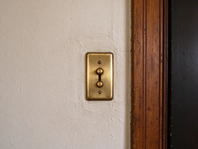 An old push-button light switch in a brass cover plate beside a stained wood door frame